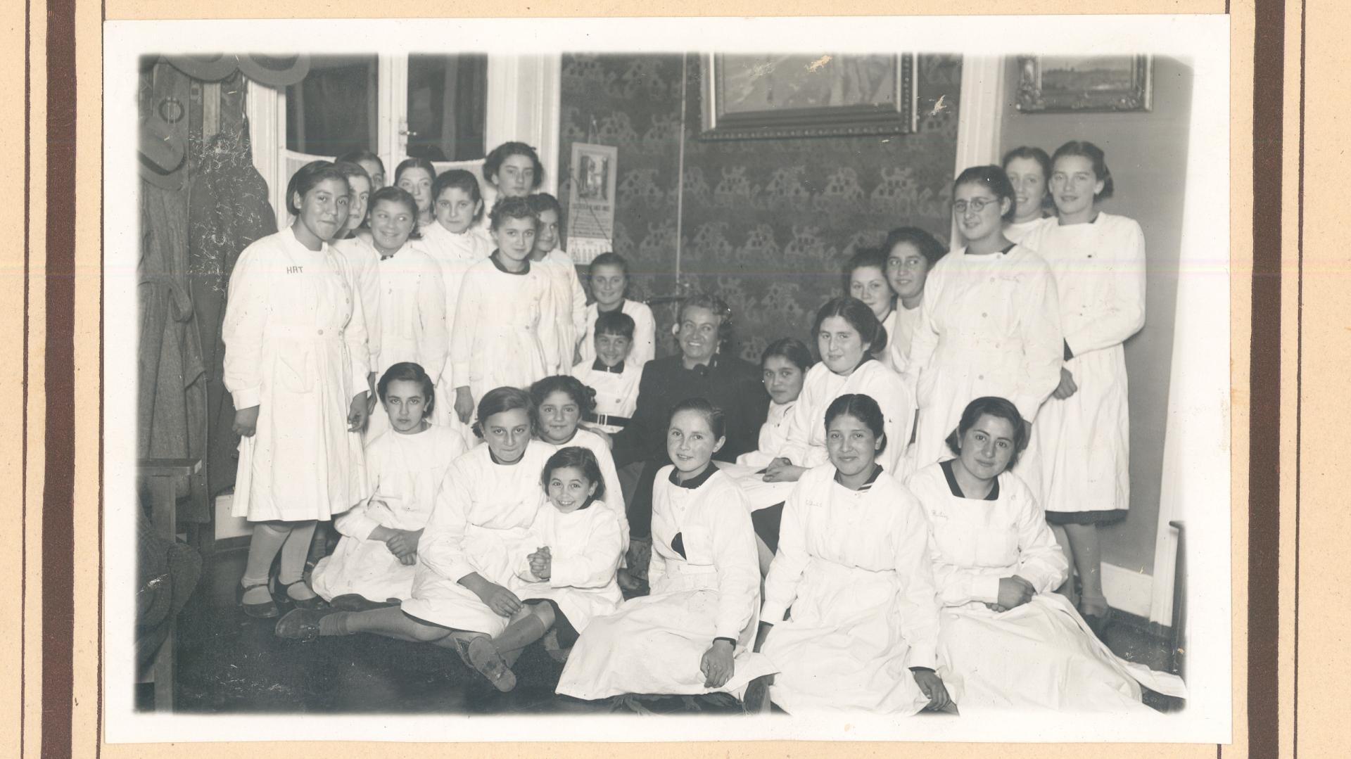 Gabriela Mistral sentada, rodeada de alumnas con delantal blanco.