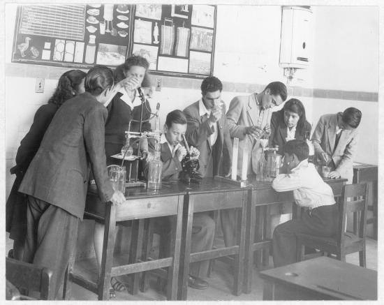 Gurpo de estudiantes escolares, hombres y mujeres, en una sala con material de laboratorio.